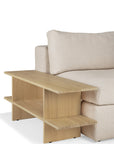 A beige upholstered sofa pairs with the Ethnicraft Kabuki Side Table – Oak, featuring two open shelves and a modern minimalist look. Crafted from solid oak, the table aligns seamlessly with the sofa’s armrest for style and function.