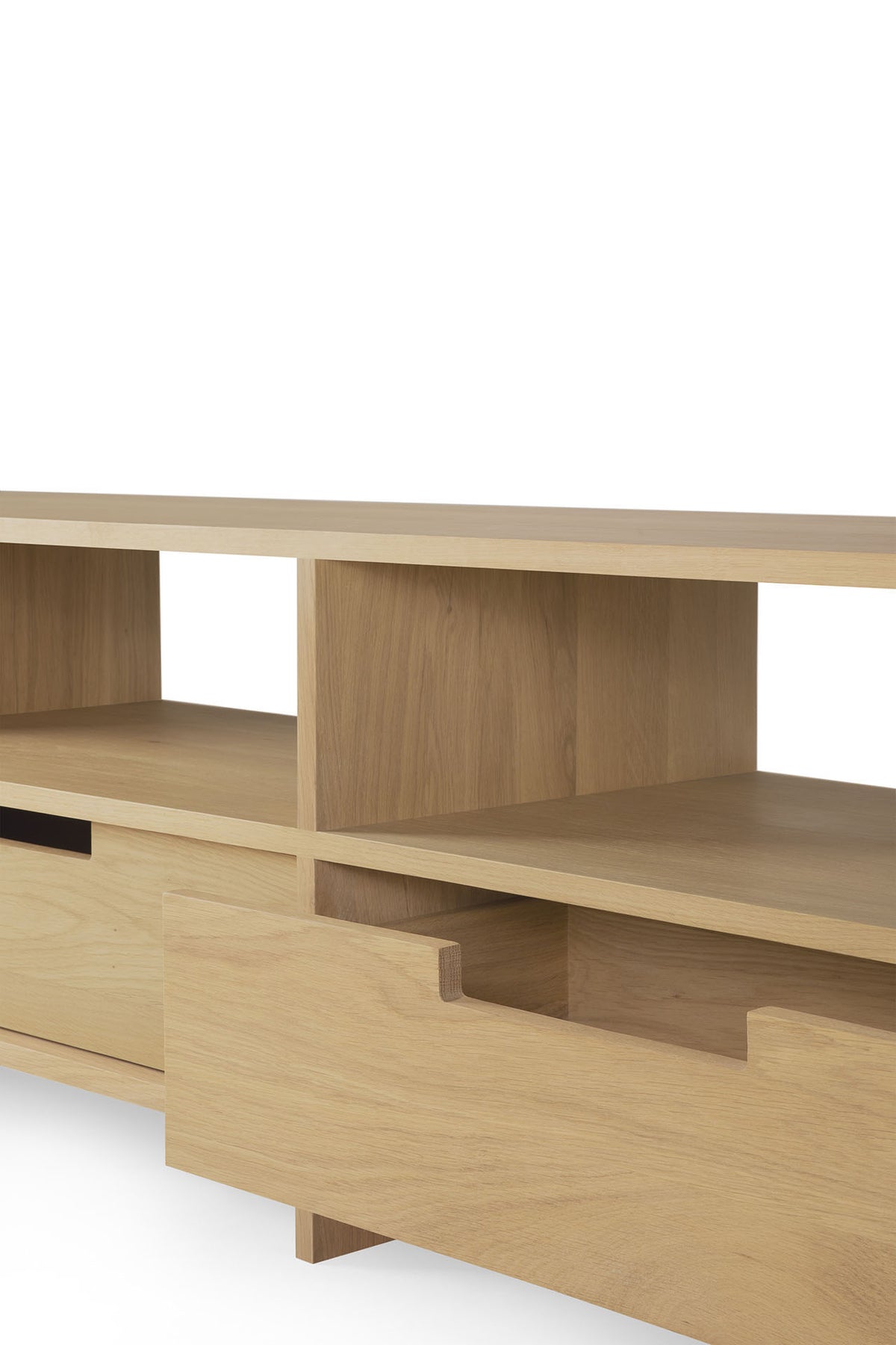 A light oak TV stand crafted by Ethnicraft, the Kabuki TV cupboard features open shelving and a partially open lower drawer, its minimalist silhouette displayed against a white background.