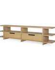 The Ethnicraft Kabuki TV cupboard in oak showcases a minimalist, modern design characterized by clean horizontal lines and a sleek varnished oak finish. Featuring two open shelves on each side and two central drawers with rectangular black handles, this timeless piece brings the signature Ethnicraft aesthetic to any living room.