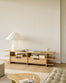 Minimalist living room with light wood furniture, featuring an Ethnicraft Kabuki TV cupboard in oak, a sculptural white lamp, books, and ceramic decor on a low shelf. Neutral tones, soft lighting, and clean lines create a calm, modern atmosphere.