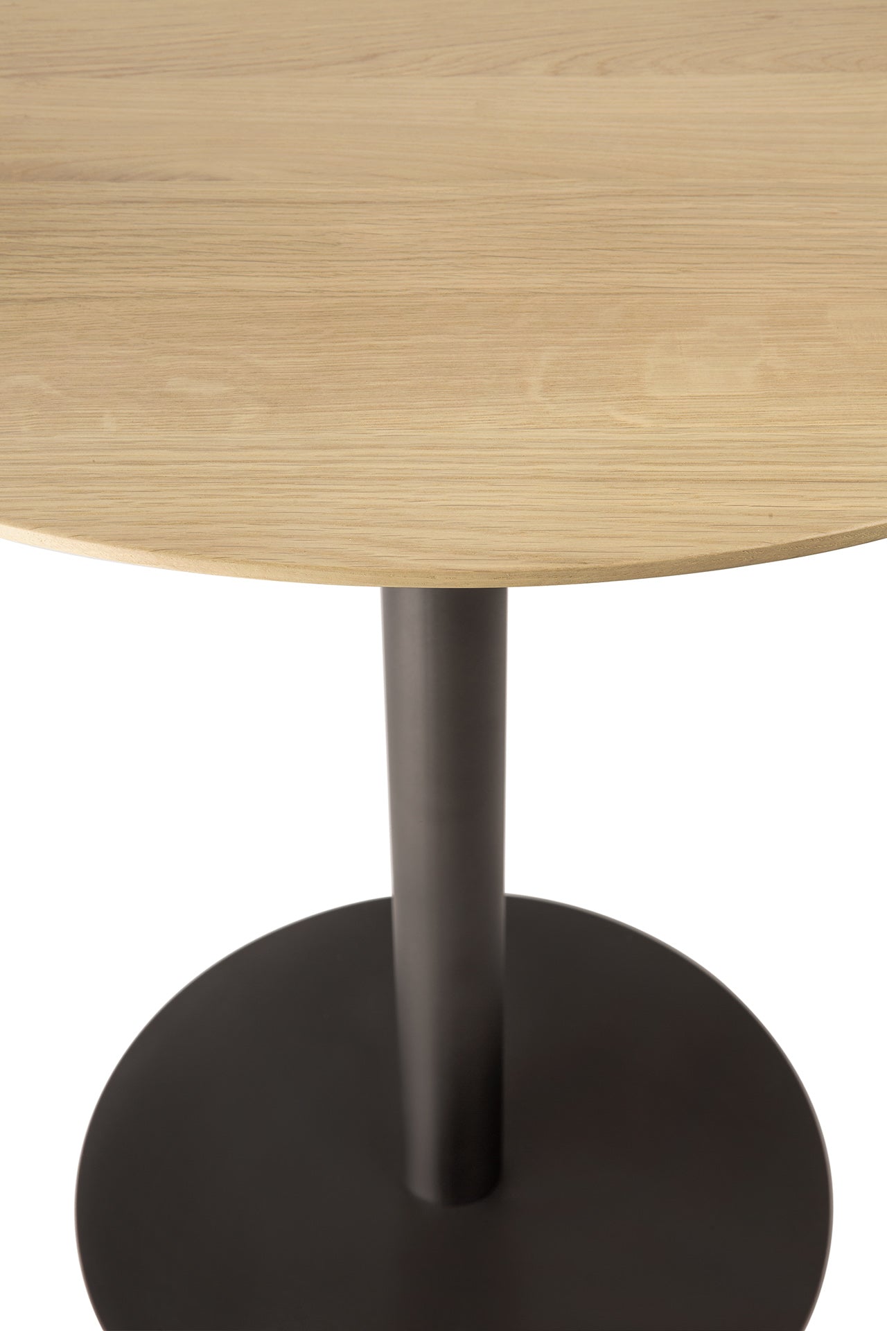 A close-up of the Ethnicraft Blend Dining Table - Oak shows its round solid oak top with a light finish and a single black metal pedestal base on a circular bottom, set against a white background.