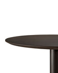 A close-up of the Ethnicraft Blend Dining Table - Brown Oak shows its round dark wood top and single cylindrical pedestal base against a plain white background.