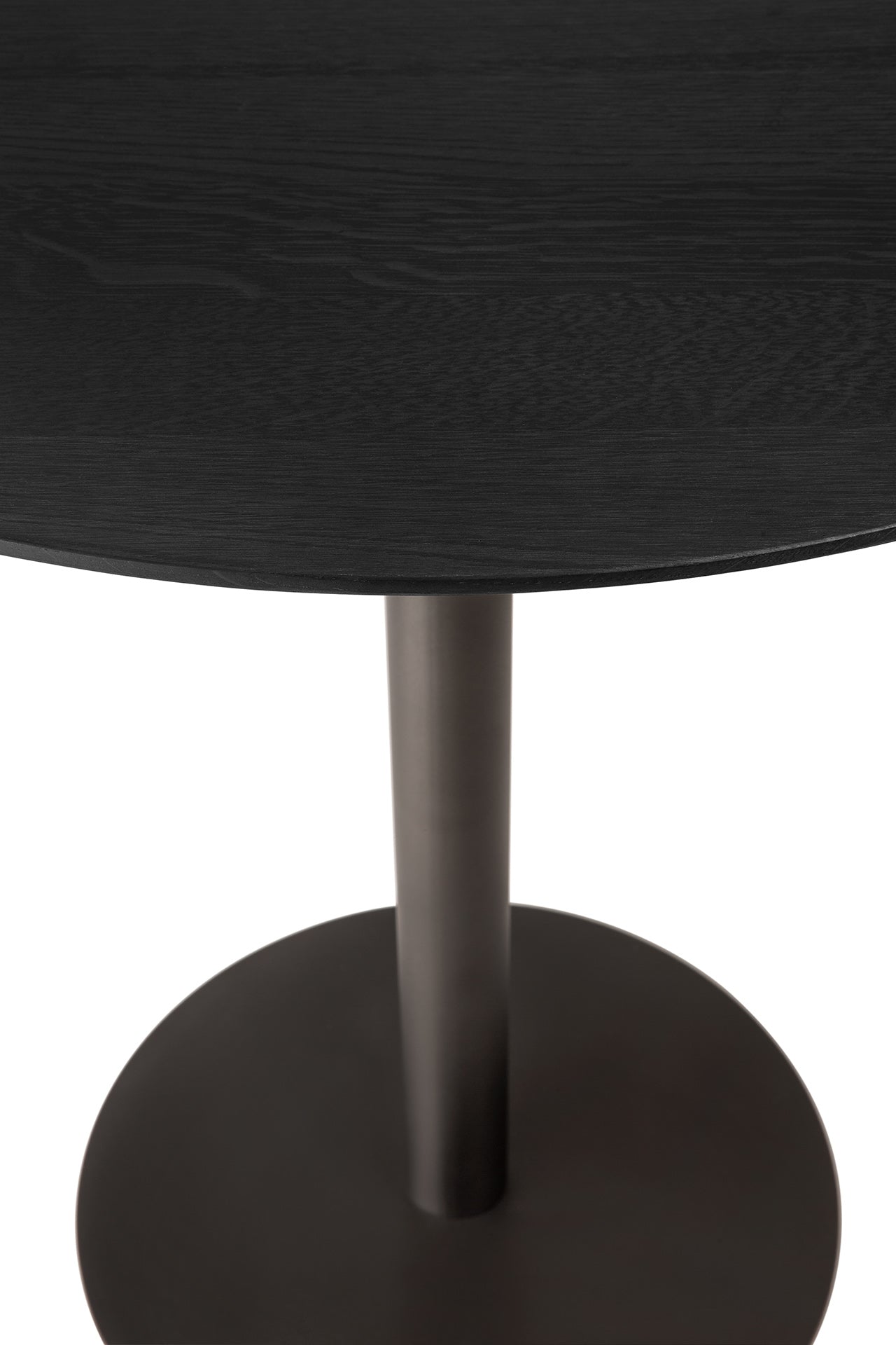A close-up of the Ethnicraft Blend Dining Table - Black Oak highlights its round solid oak tabletop and metal pedestal base, set against a white background.