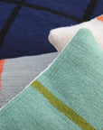 Three decorative pillows overlap: Ania Brzeski’s Pillow 07 in jade and olive stripes, a dark blue pillow with black modernist lines, and a cream pillow with orange and light blue stripes.