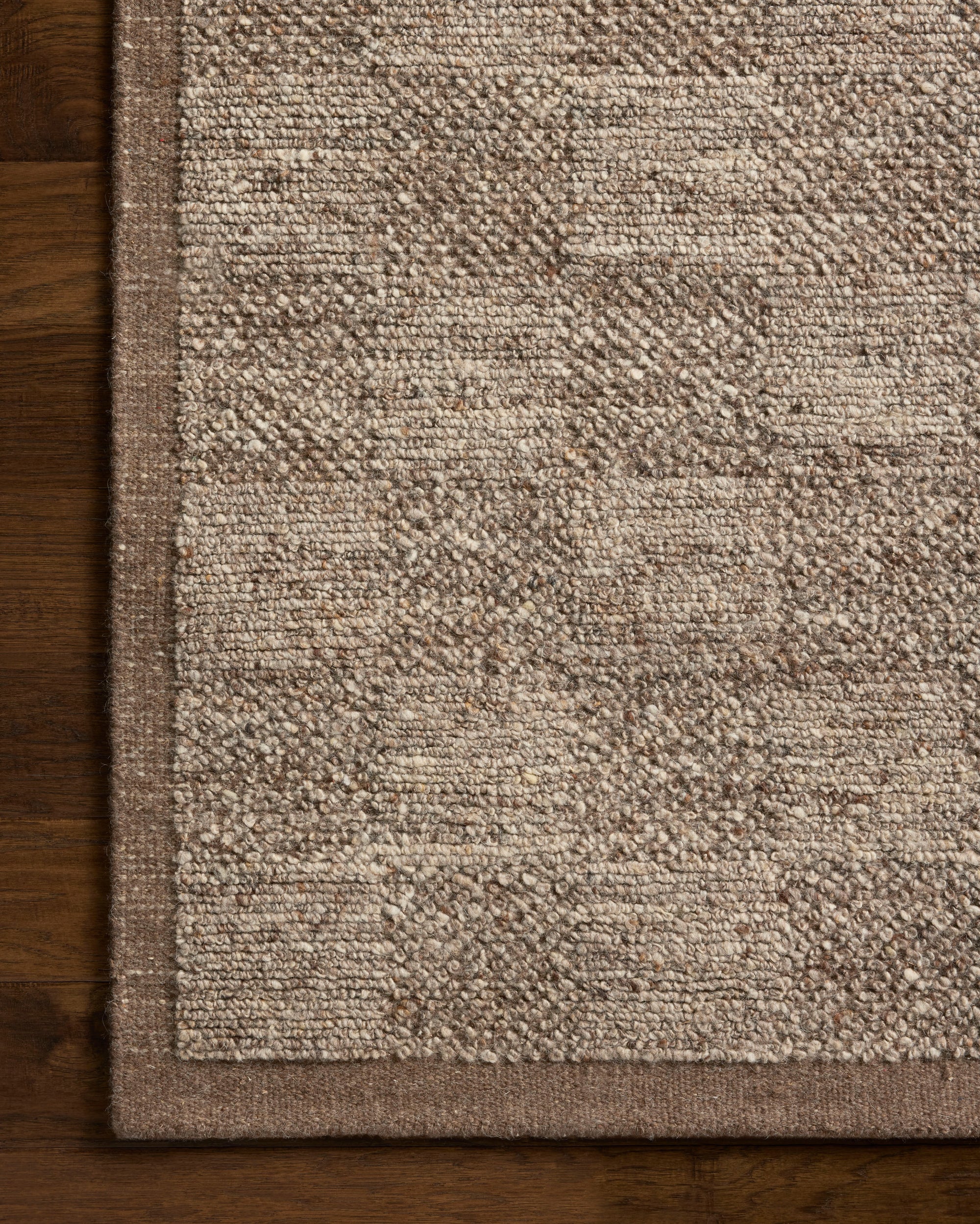 A close-up of the Loloi Alina Rug - Bark showcases its hand-woven checkerboard pattern in beige and light brown, bordered by a solid brown edge, resting on a dark wooden floor.