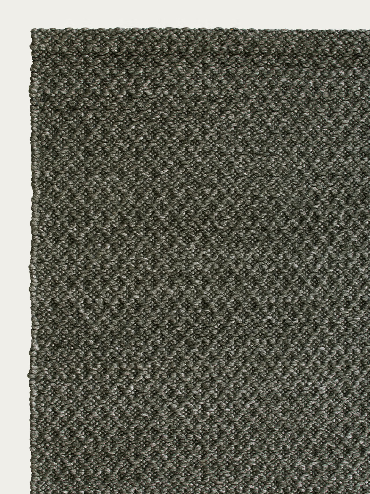 Close-up of the Armadillo&amp;Co Sherpa Rug - Kelp, featuring a textured, dark gray hand-woven wool surface with a tightly stitched pattern; the top left corner and edges are shown against a white background.