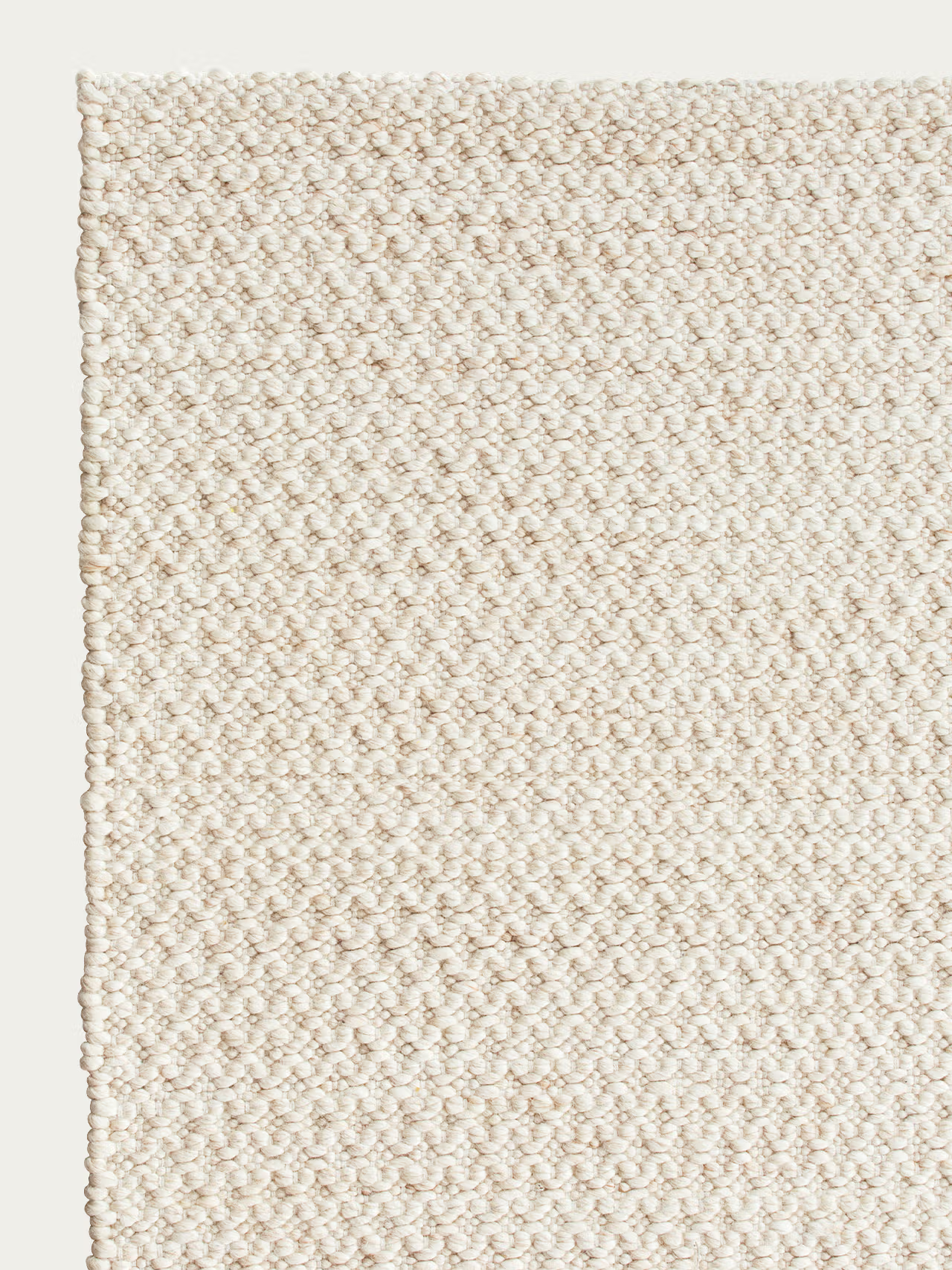 Close-up of the Sherpa Rug - Sand by Armadillo&amp;Co, showcasing its textured, off-white handwoven wool with a subtle diamond pattern and a finished edge on the left side against a plain background.