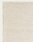 Close-up of the Sherpa Rug - Sand by Armadillo&Co, showcasing its textured, off-white handwoven wool with a subtle diamond pattern and a finished edge on the left side against a plain background.