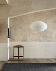 A minimalist room with textured beige walls features the Sherpa Rug in Charcoal by Armadillo&Co, accompanied by a small wooden table and a large white paper lantern pendant light hanging from the ceiling.