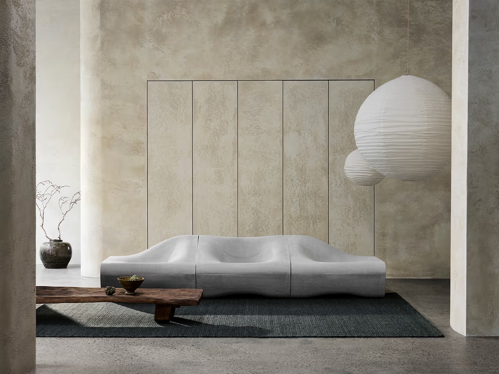 Minimalist living room with a sculptural white sofa, large paper lanterns, a low wooden coffee table, a small vase with twigs, and textured beige walls for a calm, modern atmosphere. The space is anchored by the Sherpa Rug – Kelp from Armadillo&amp;Co, its hand-woven wool design adding warmth and artisanal character to the serene setting.
