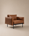 The Attendant Lounge Chair | Leather by Wooden Stories features brown leather upholstery, square cushions, wide armrests, and a black metal frame, set against a plain beige background.