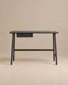 A minimalist black oak Author Desk from Wooden Stories, part of the Danish collection, featuring a small central drawer and set against a plain beige background.