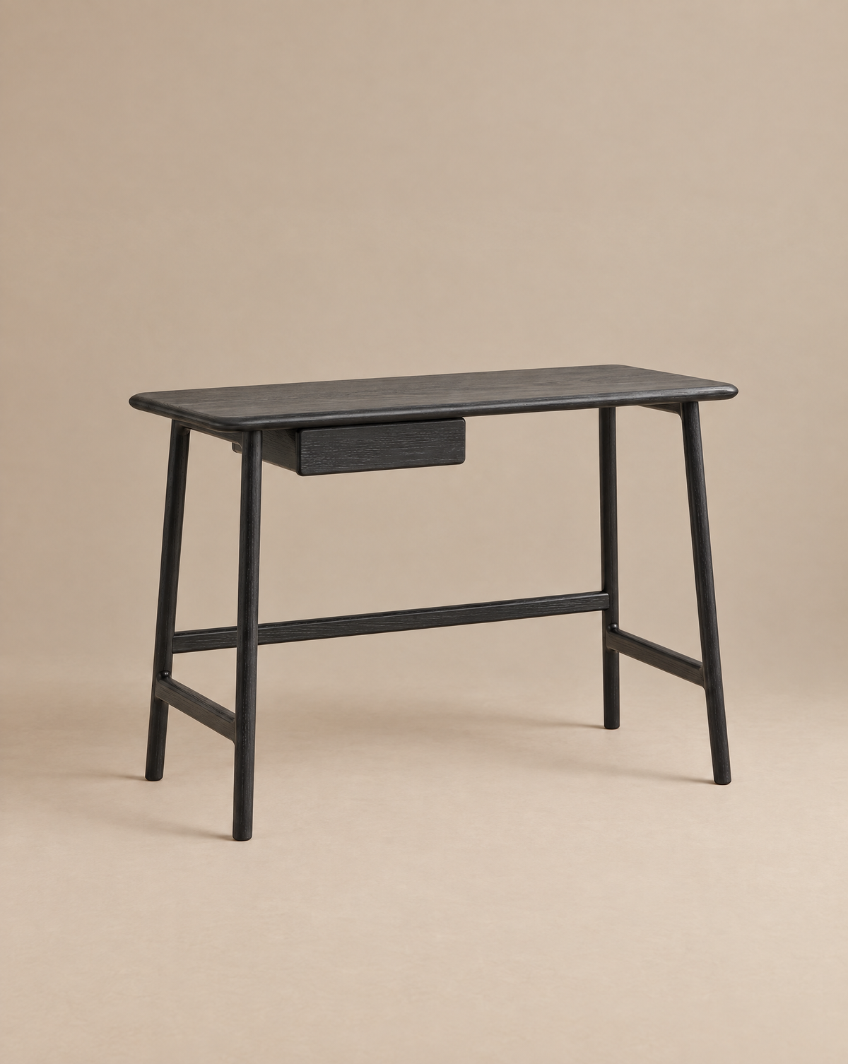 The Wooden Stories Author Desk in black oak features angled legs and a single central drawer, its sleek Danish-inspired lines highlighted against a plain beige background.