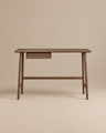 The Author Desk | Espresso Oak by Wooden Stories features a minimalist solid wood design with smooth edges, a small centered drawer, and distinctive angled legs. As part of the Danish collection, it’s an excellent choice for your home office furniture. The warm beige background complements the desk’s espresso oak finish, creating a cohesive and inviting look.