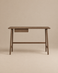 The Author Desk | Espresso Oak by Wooden Stories features a minimalist solid wood design with smooth edges, a small centered drawer, and distinctive angled legs. As part of the Danish collection, it’s an excellent choice for your home office furniture. The warm beige background complements the desk’s espresso oak finish, creating a cohesive and inviting look.