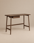 The Author Desk | Espresso Oak by Wooden Stories is crafted from solid wood and features a single central drawer, simple clean lines, and slightly angled legs. Set against a plain beige background, it’s an elegant addition to any Danish-inspired home office collection.