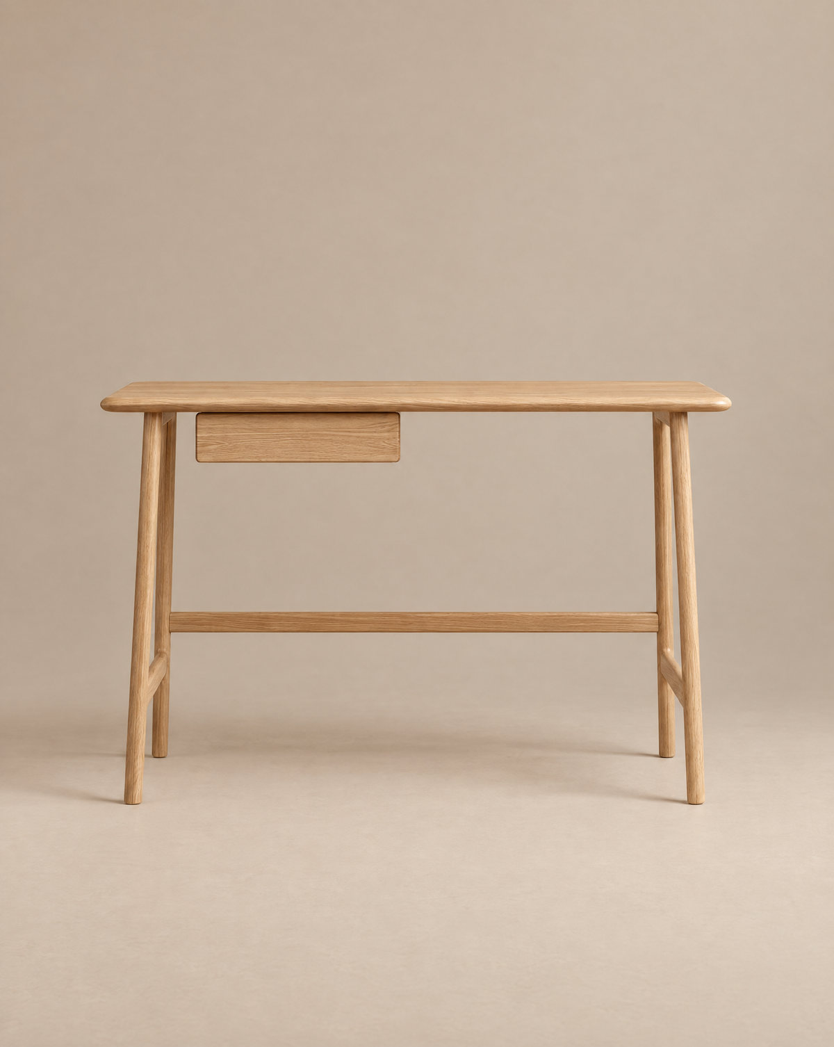 The Author Desk | Light Oak by Wooden Stories is a minimalist Danish office desk, expertly crafted from solid wood. It features four rounded legs, a flat rectangular tabletop, and a small drawer on the left side. Set against a plain beige background, the neutral tones of this refined desk create an elegant and understated workspace.
