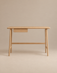 The Author Desk | Light Oak by Wooden Stories is a minimalist Danish office desk, expertly crafted from solid wood. It features four rounded legs, a flat rectangular tabletop, and a small drawer on the left side. Set against a plain beige background, the neutral tones of this refined desk create an elegant and understated workspace.
