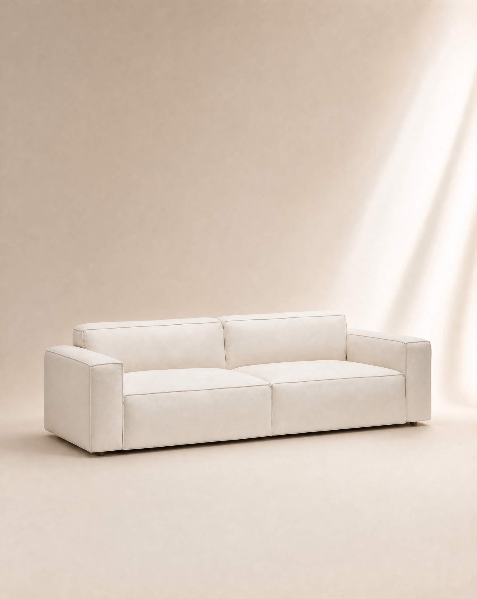A modern, minimalist Baker Sofa | Fabric by Wooden Stories, featuring wide armrests and low backrests in a cream color, sits on a light beige background with soft natural lighting.