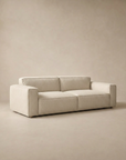 The Baker Sofa | Fabric by Wooden Stories features a modern, low-profile Danish design with feather filling, wide armrests, and clean lines, set against a matching beige background.