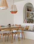Minimalist dining area featuring the Ethnicraft Bok Dining Table in oak, pendant lamps, and a built-in bench with patterned and solid cushions. An arched wall niche displays books and decor in warm, neutral hues.