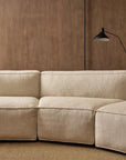 The Baker Modular Sofa | Fabric • M9 by Wooden Stories, with clean lines and customizable sections, sits on a textured rug against a wooden wall. A black wall-mounted reading lamp is above the sofa’s right side.