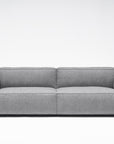 The Baker Sofa | Fabric by Wooden Stories features a contemporary gray design with wide armrests, a low backrest, and plush feather filling, displayed against a plain white background.