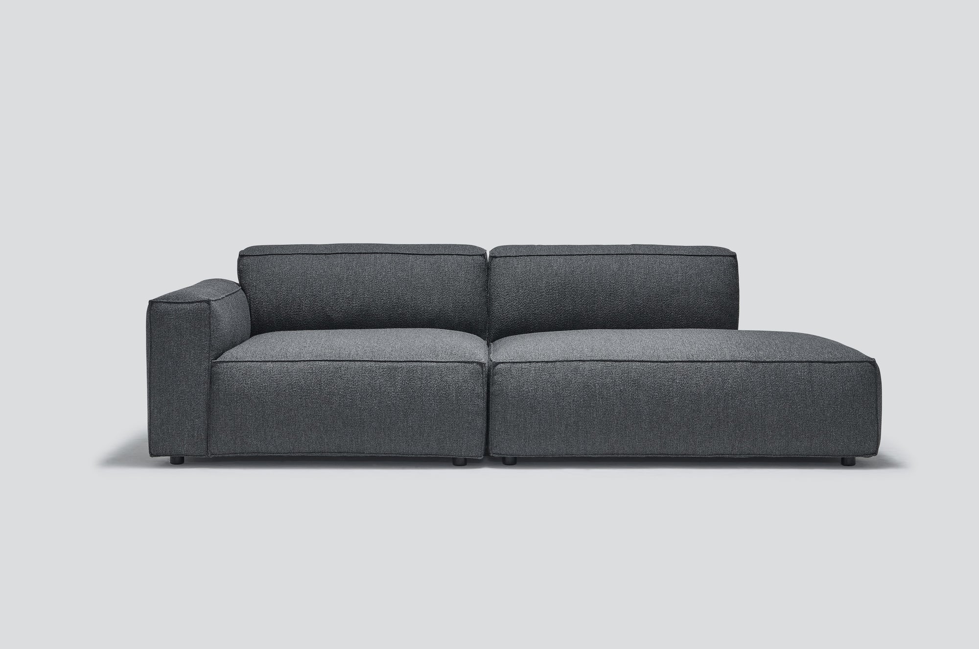 The Baker Modular Sofa | Fabric • M1 by Wooden Stories is a modern, dark gray sectional with a left armrest and spacious seating, shown against a plain light gray background.