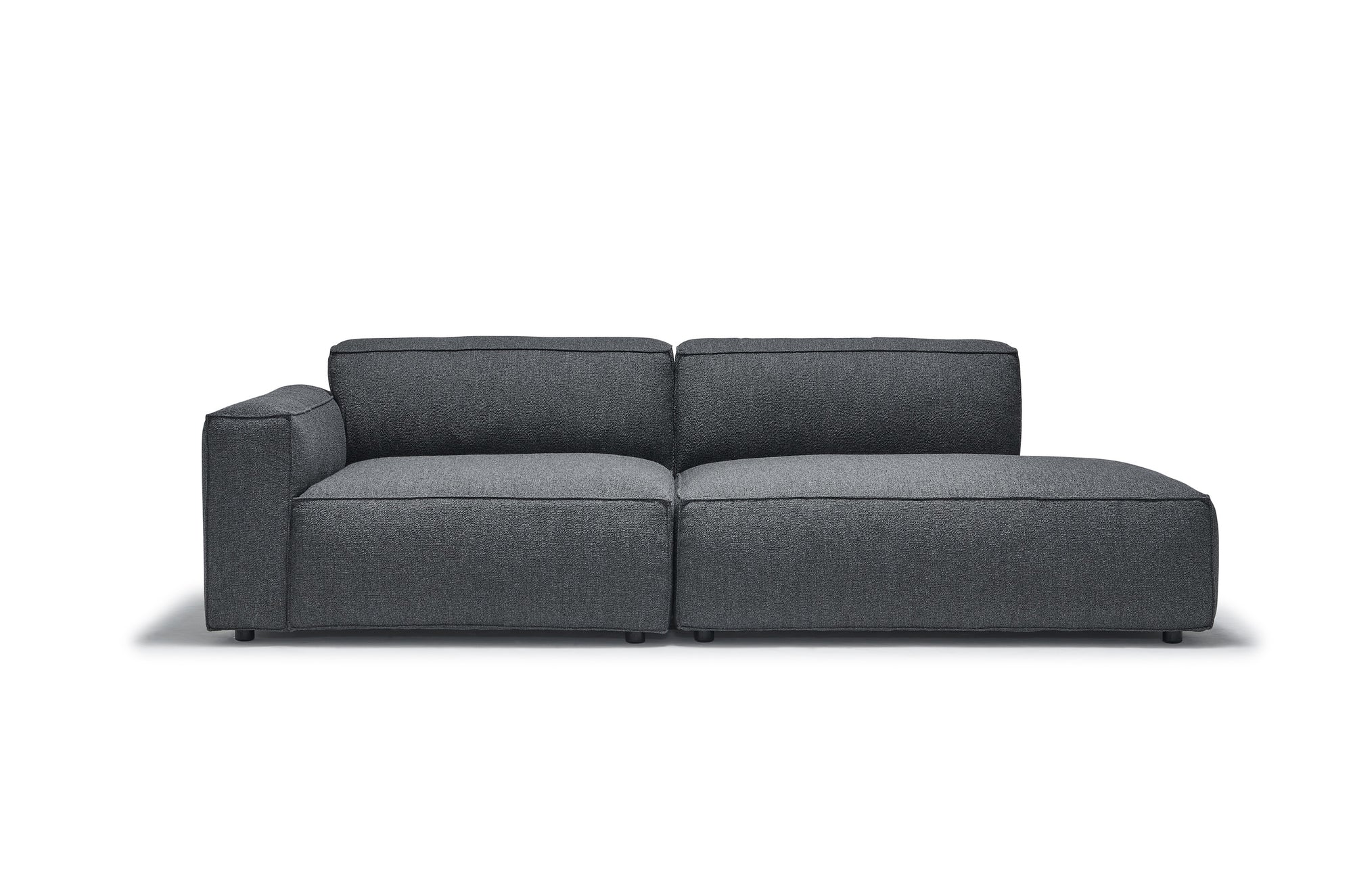 The Baker Modular Sofa | Fabric • M1 by Wooden Stories is a contemporary dark gray modular piece with a left armrest and wide, deep feather-filled cushions, shown against a plain white background.