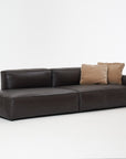 The Baker Modular Sofa | Leather • M2 by Wooden Stories is a modern dark brown leather sofa with two light brown throw pillows, showcased against a plain white background.