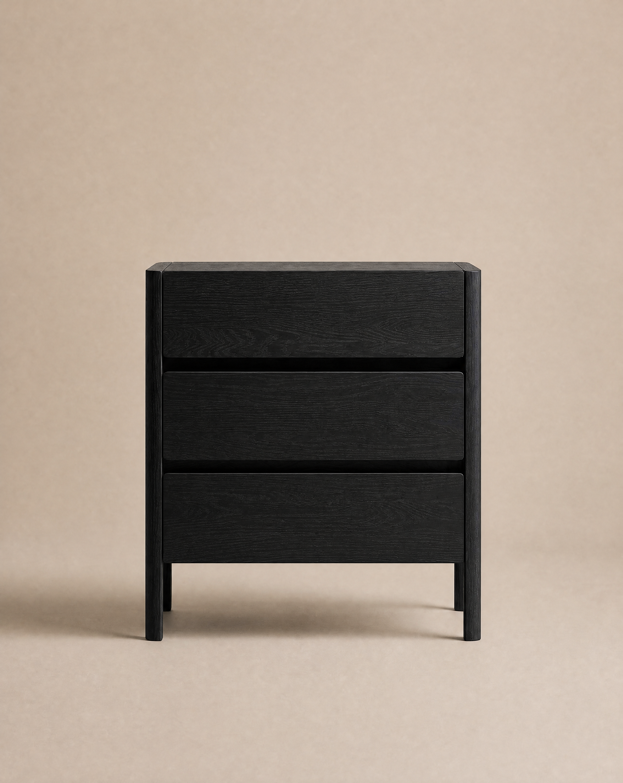The Nell Tall Dresser by Wooden Stories, part of the Danish Collection, is a modern black wooden nightstand featuring three drawers with clean lines, premium metal runners, and a handleless design. Shown against a plain beige background, it offers stylish yet practical storage for your bedroom.