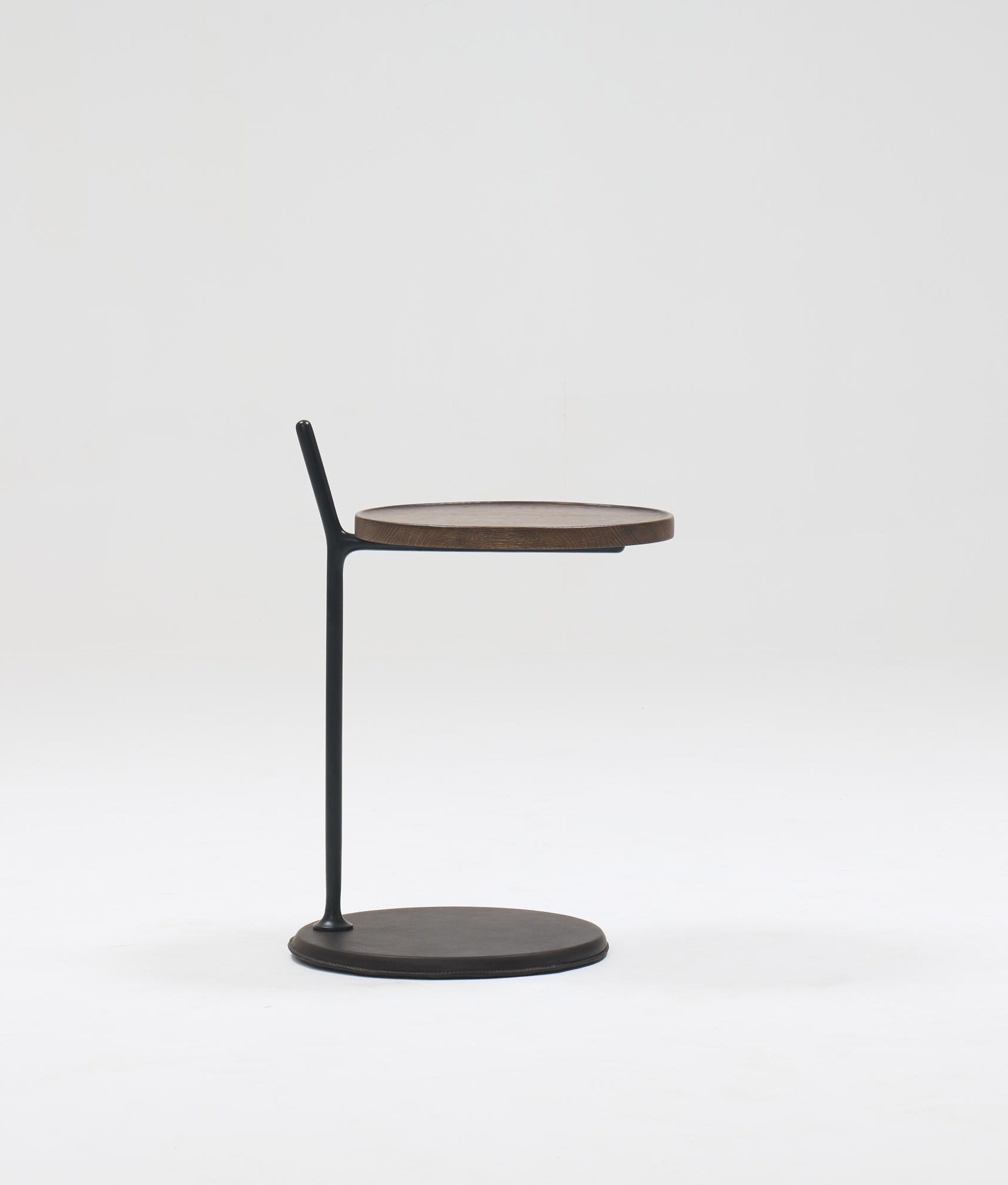 The Bystander Side Table by Wooden Stories features a round wooden top, slim black vertical support, and round black base, shown against a plain white background for a minimalist look.