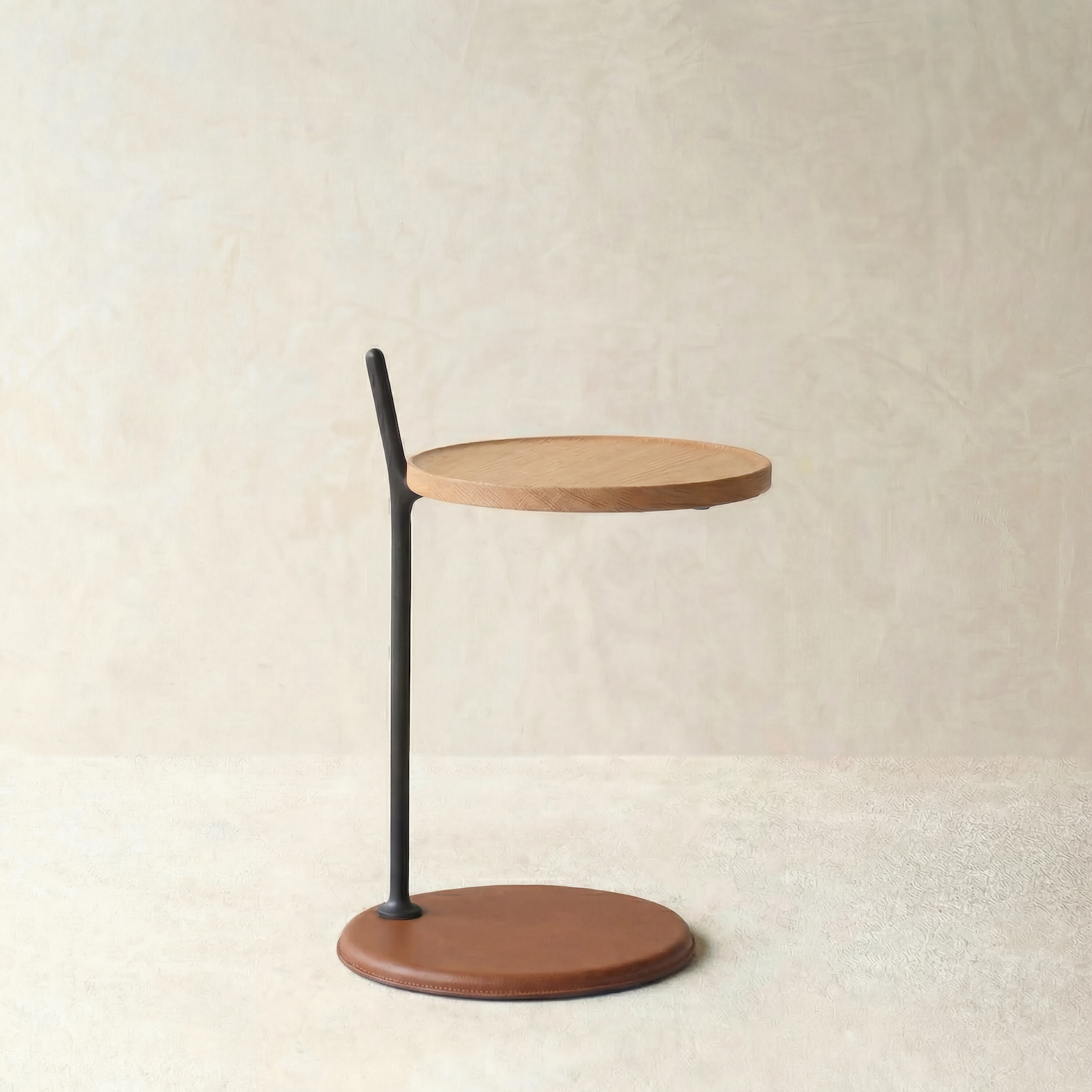 The Wooden Stories Bystander Side Table features a modern, minimalist design with a solid wood top, slim black metal support, and circular brown base from the Danish Collection, set against a neutral textured background.