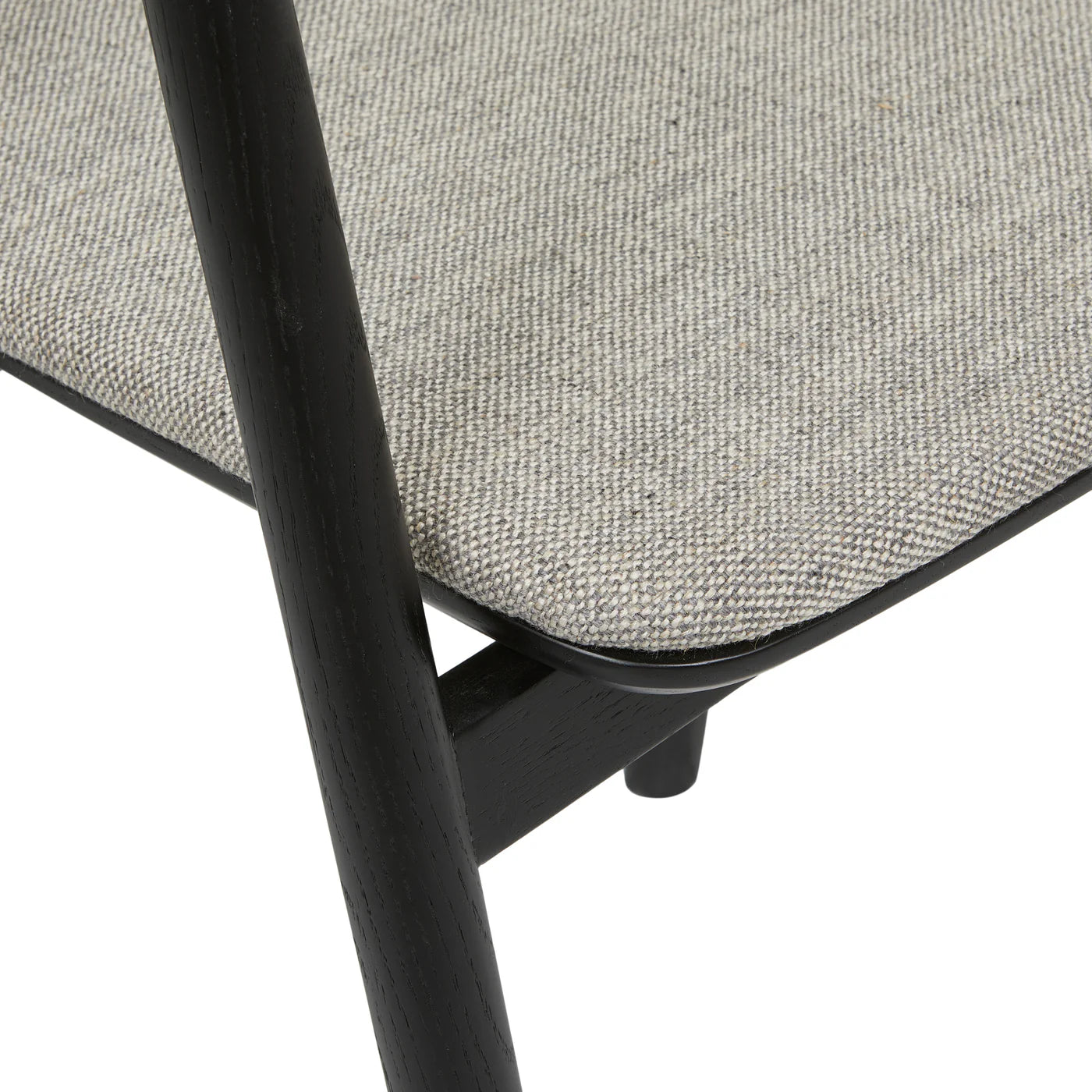 Close-up of the Wooden Stories Inlay Dining Chair, featuring light gray textured fabric upholstery and a black oak frame, focusing on the corner where the seat meets the leg.