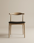 The SOBU Copenhagen Dining Chair - White Ash features a modern curved backrest and black leather seat, set against a beige background. Its minimalist look draws inspiration from Scandinavian and mid-century design.