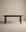 The Cove Dining Table | Black Oak by Wooden Stories, featuring a minimalist design with rounded corners and four cylindrical legs in solid American oak, stands in an empty room with plain beige walls and floor.