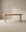 The Wooden Stories Cove Dining Table | Light Oak features solid American oak with rounded edges and four cylindrical legs, shown against a neutral beige background in a softly lit room.