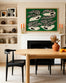 A modern dining room with a wooden table, SOBU’s Copenhagen Dining Chairs in Black Ash with leather seats, an orange vase with foliage, green art above a white fireplace, shelves of pottery and framed art, and two orange candles on the mantel.