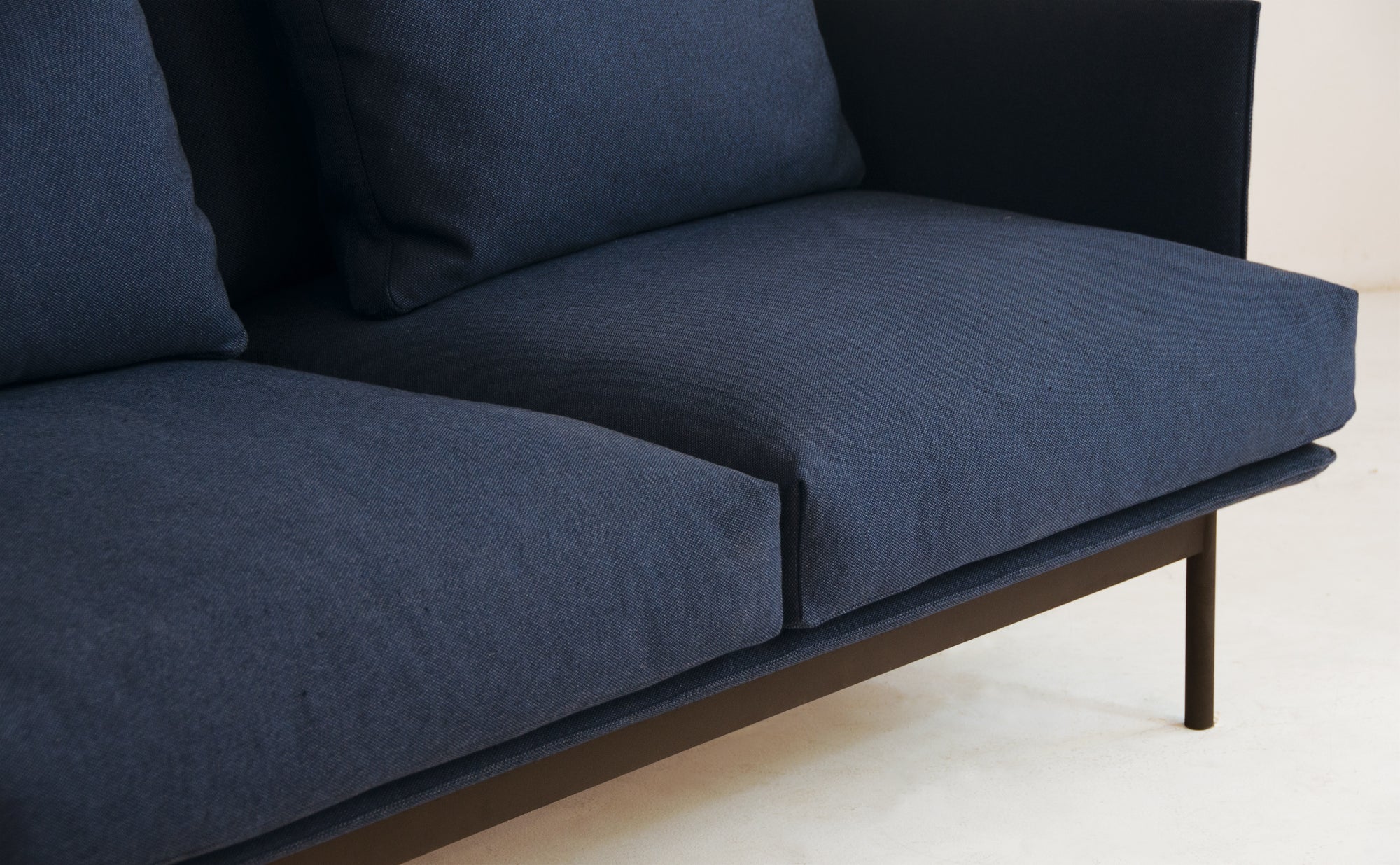 Close-up of the Cherry Sofa 95" by Wooden Stories, featuring dark blue fabric upholstery, two seat cushions, Danish-inspired lines, and slim dark metal legs—ideal for a modern living space with a light-colored floor.