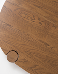 A close-up of a round wooden table crafted from solid American oak in the warm Latte Oak finish, with visible wood grain and a small circular protrusion on the edge—highlighting the contract-grade quality of the Cove Dining Table by Wooden Stories.