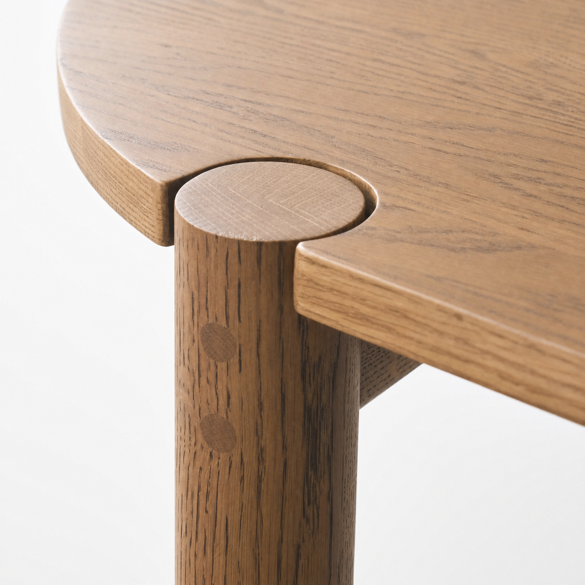 Close-up of the Cove Dining Table | Latte Oak by Wooden Stories, highlighting a round leg seamlessly integrated into the edge of the tabletop, with visible wood grain and joinery details crafted from solid American oak.
