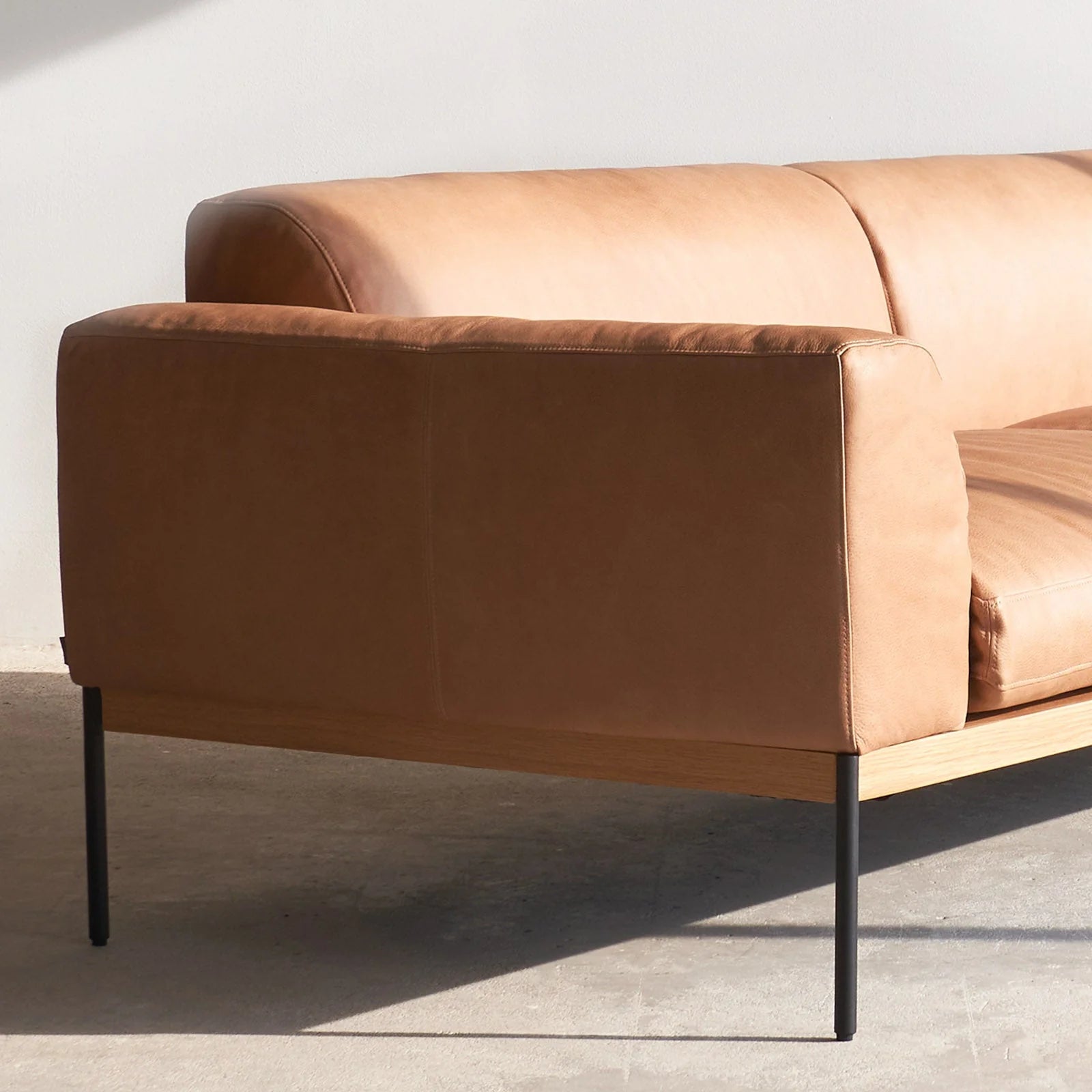 The Department Modular Sofa | Leather • M5 Right by Wooden Stories features modern tan leather, slim black metal legs, and an FSC-certified oak base. It sits on a concrete floor against a plain white wall in natural light.