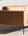 The Department Modular Sofa | Leather • M5 Right by Wooden Stories features modern tan leather, slim black metal legs, and an FSC-certified oak base. It sits on a concrete floor against a plain white wall in natural light.