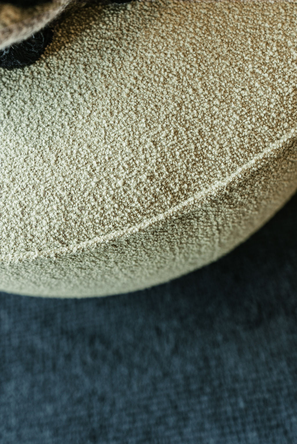 Close-up of a beige textured cushion on a dark fabric, showcasing detailed stitching and Danish-inspired lines, reminiscent of the Wooden Stories Fable Ottoman | Fabric.