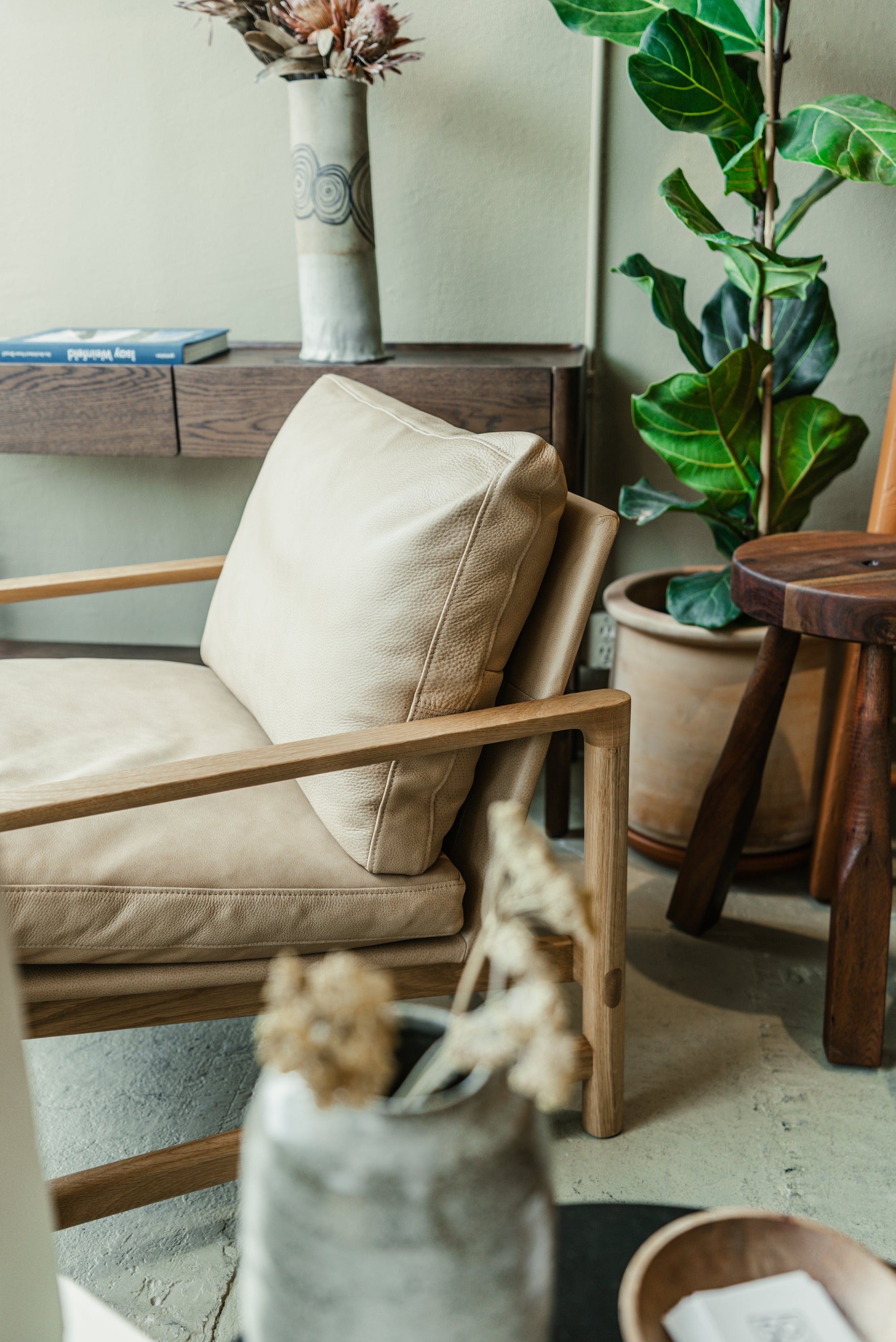 Beige Troubador armchair with wooden frame in a room with plants and a shelf.