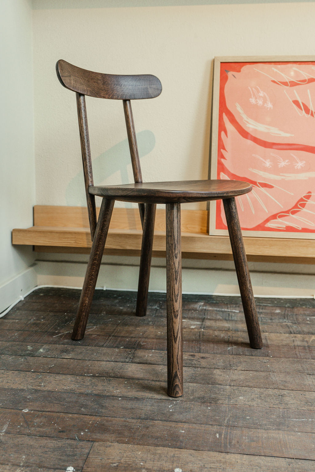 Wooden Figura chair on a wooden floor with a colorful abstract painting in the background.