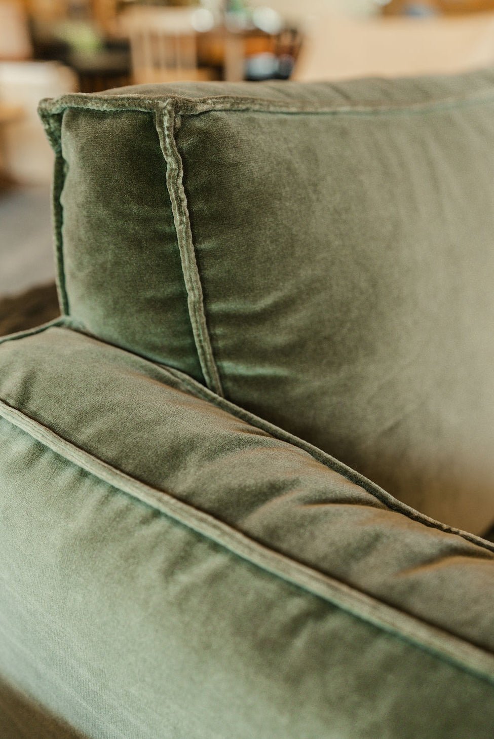 Close-up of Wooden Stories’ Attendant Lounge Chair | Fabric in green velvet, showcasing the plush upholstery and detailed seams on the backrest and armrest, set against a softly blurred background.