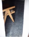 A wooden chair with beige cushioning is partially visible behind white curtains, set on a textured gray Radhi Rug - Silver by HIMALAYAN HERMITAGE.