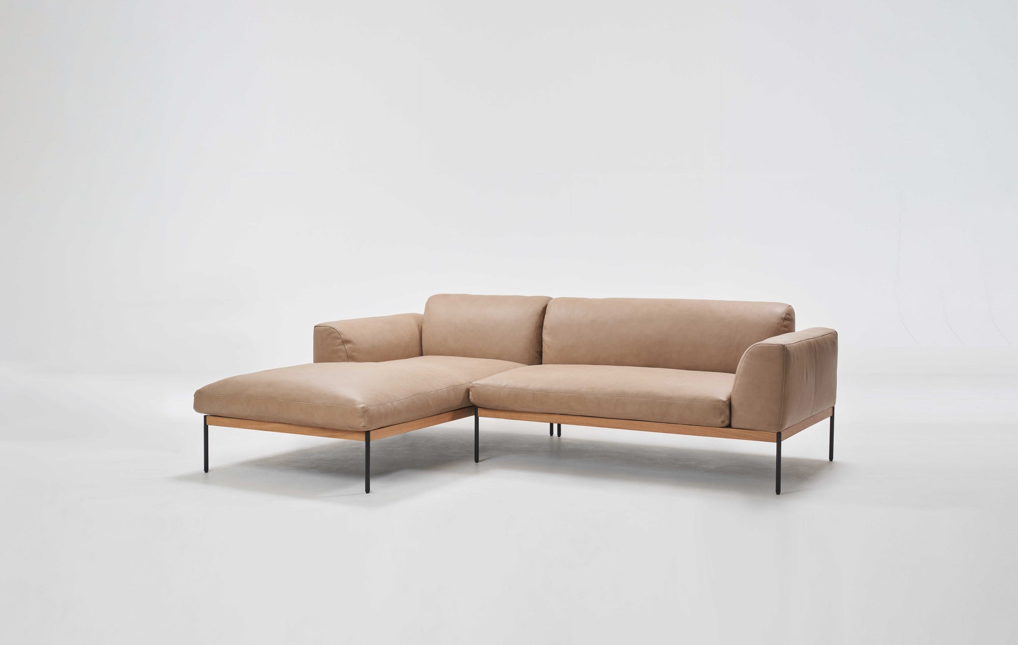 The Department Modular Sofa | Leather • M1 Left by Wooden Stories features a modern beige L-shape, low solid wood base, and slim black metal legs, inspired by Danish design, set against a plain white background.