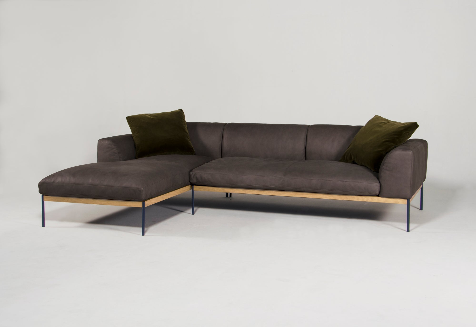 The Department Modular Sofa | Leather • M2 Left by Wooden Stories features dark gray upholstery, two olive green cushions, slim black metal legs, and an FSC-certified oak base, set against a plain white background.